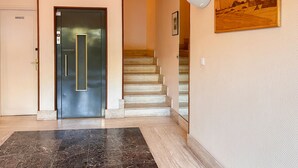 Un intérieur moderne avec un hall d’entrée en marbre, une porte en acier inoxydable, un escalier et un luminaire fixé au mur.