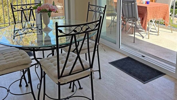 Un espace de restauration moderne avec des tables et des chaises en verre, une vue sur un jardin luxuriant et un balcon doté de sièges extérieurs.