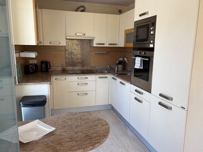 Une cuisine compacte avec des meubles blancs, un plan de travail en granit, un four encastré et une petite poubelle.