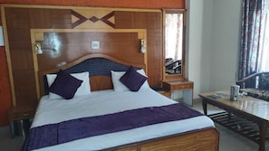 A hotel room with a wooden headboard, a bed with white and purple bedding, a small bedside table, and a wooden nightstand.
