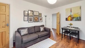 Een woonkamer met een grijze bank, een eettafel met stoelen en kunstwerken in lijsten aan de muur.