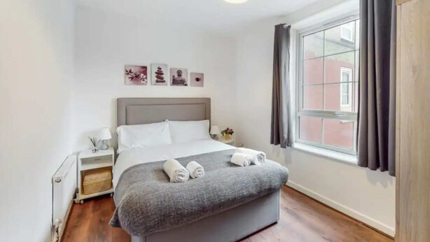 Een netjes ingerichte slaapkamer met een bed, nachtkastjes, een raam met gordijnen en kunst aan de muur.