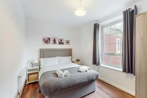 A neatly arranged bedroom with a bed, bedside tables, a window with curtains, and artwork on the wall.