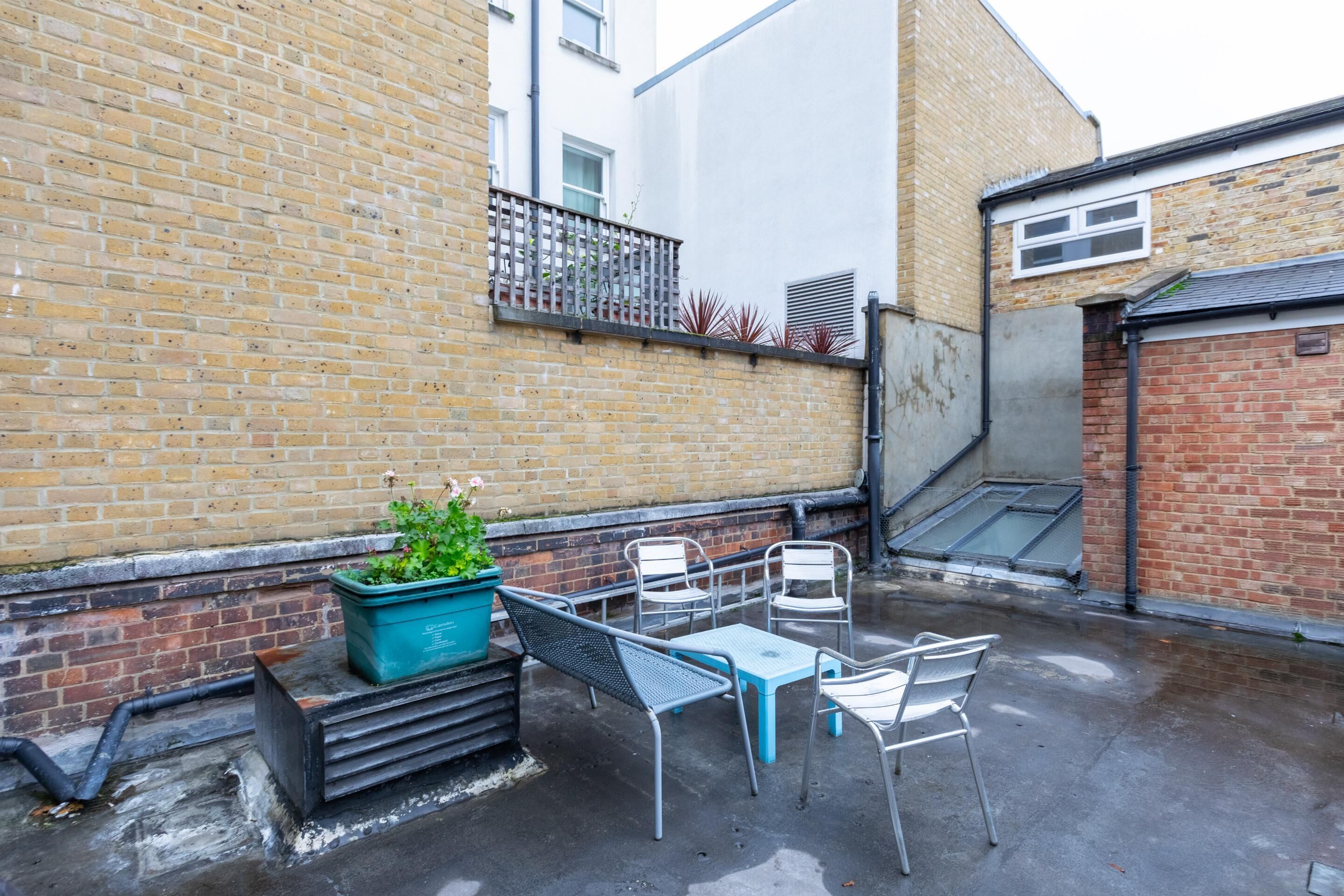 A patio area with a brick wall, a metal table and chairs, and a potted plant.