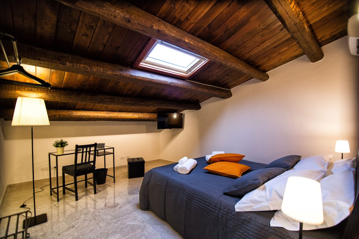 A bedroom with a bed, a desk, a chair, and a skylight.