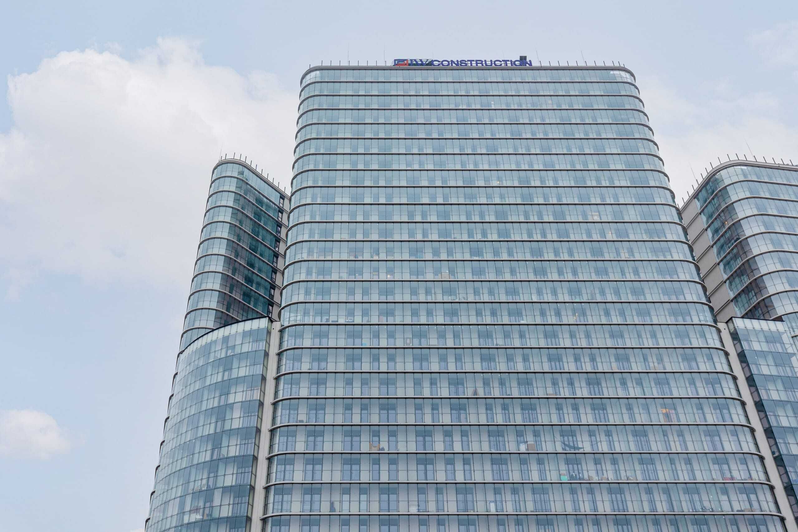 A tall, curved glass skyscraper with a sign reading "EVCONSTRUCTION" at the top.
