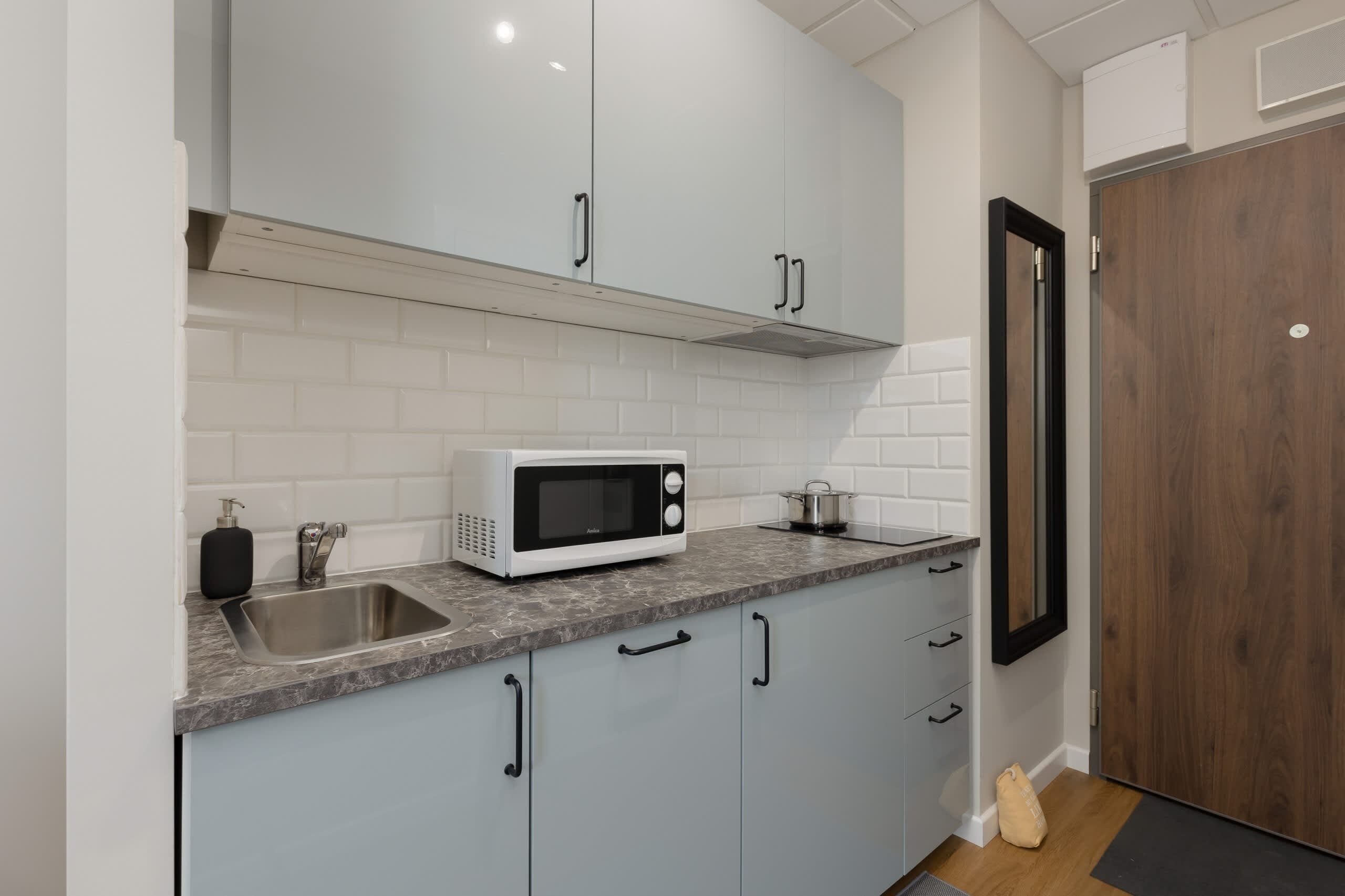 A compact kitchen with light cabinets, a microwave, and a tiled backsplash for a clean, modern look.