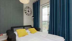 A modern hotel room with a large bed, a clock on the wall, and a view of the city through the window. - Compact Studio in Wola | Balcony | Air Conditioning (Warszawa)