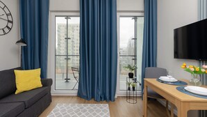 A modern living room with a sofa, dining table, and large windows with blue curtains. - Compact Studio in Wola | Balcony | Air Conditioning (Warszawa)