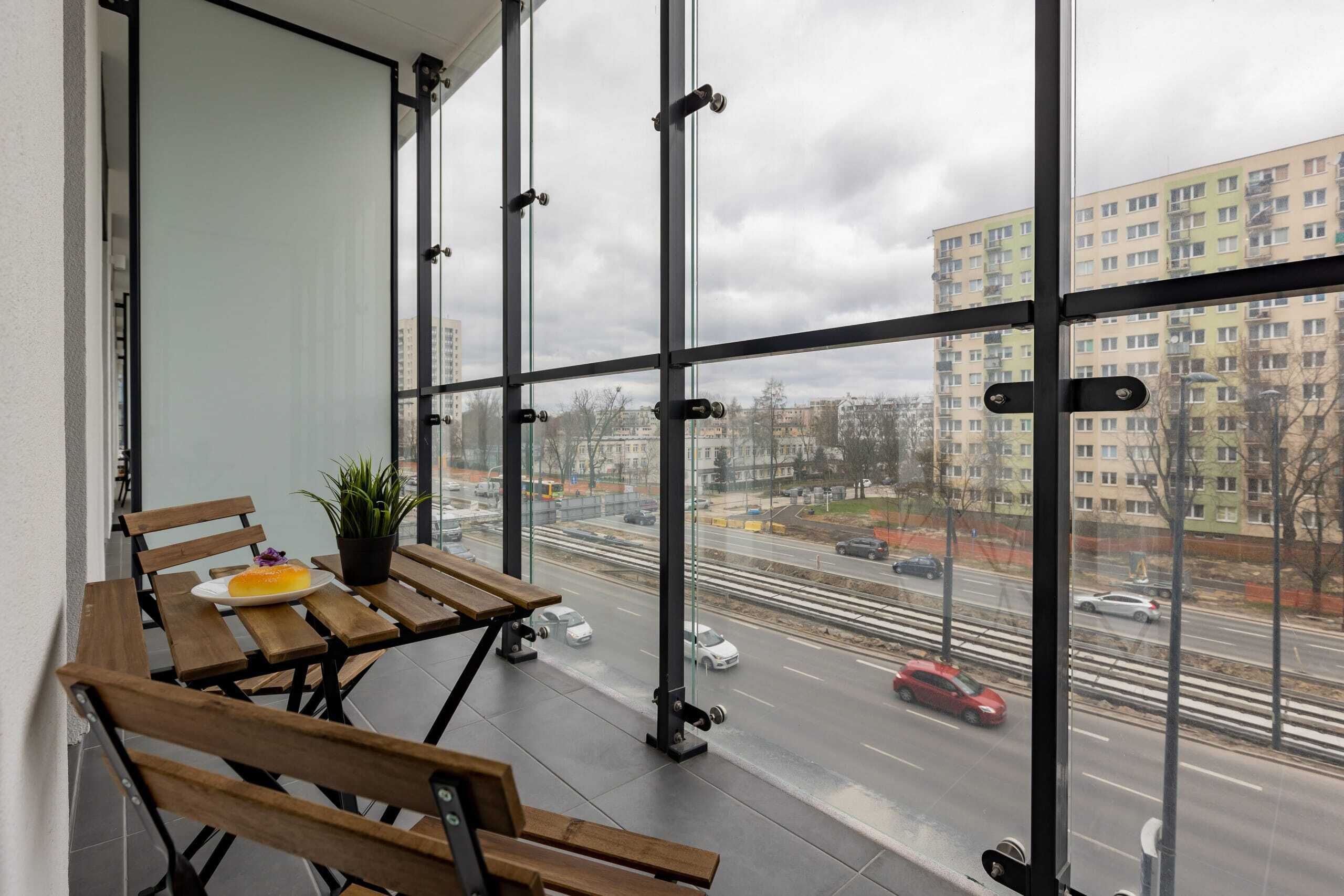 A balcony with a wooden table, a potted plant, and a plate with a dessert.