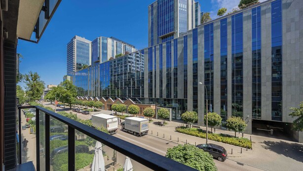 Un edificio moderno con finestre a vetro riflettente, cielo sereno e una strada con auto parcheggiate e un furgone per le consegne.