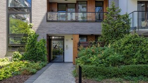Un edificio moderno con un balcone in vetro, una porta in legno e un giardino curato.