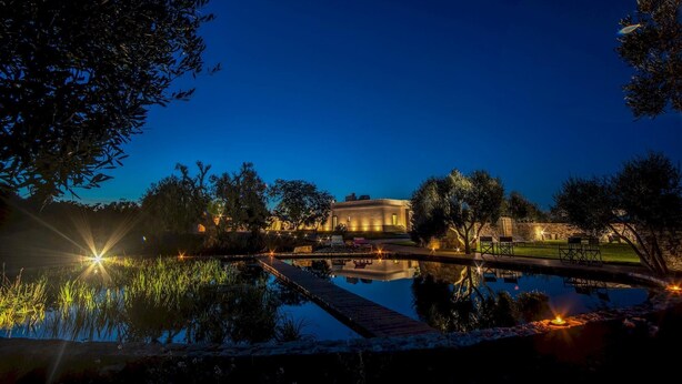 Ein Gebäude bei Nacht mit Pool und Außenbereich zum Sitzen, umgeben von Bäumen.