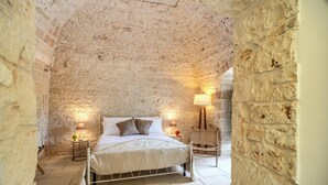 Ein Schlafzimmer mit Steinwand, einem Bett mit weißer Bettwäsche und zwei Kissen, zwei Nachttischen mit Lampen sowie einem Sessel.