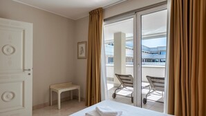 Een hotelkamer met een bed, een bankje, een stoel en een balkon met uitzicht op gebouwen.