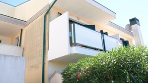 Een modern gebouw met een balkon, een heldere lucht en een groene struik op de voorgrond.