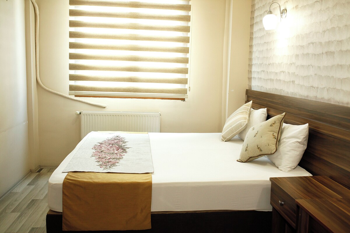 A neatly made bed with a white comforter and decorative pillows, a wooden headboard, and a bedside table with a lamp.