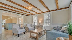 Un vaste salon doté d’un plafond en bois, d’un canapé, de fauteuils, d’une table basse et d’un coin cuisine à l’arrière-plan.