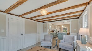 Un salon spacieux avec un plafond en bois, deux fauteuils, une table basse et une vue sur la cuisine.