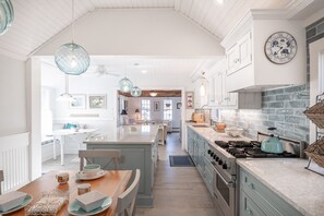 A spacious kitchen with a central island, pendant lighting, and a stone backsplash.