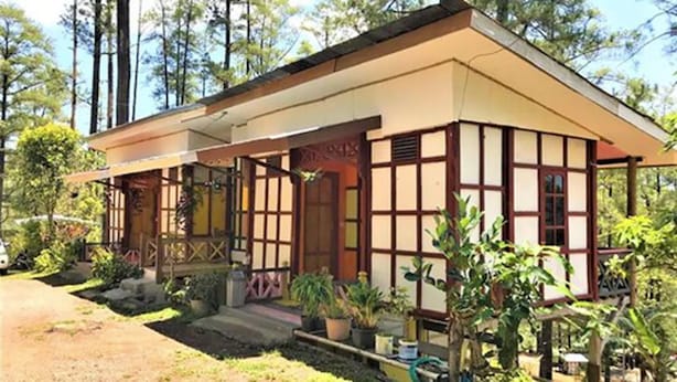 Ein traditionelles japanisches Haus mit geneigtem Dach, Holzfassade und einer überdachten Veranda mit Blumentöpfen.