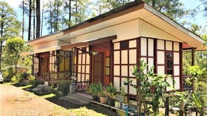Une maison traditionnelle de style japonais, avec un toit en pente, une façade en bois et une véranda couverte agrémentée de plantes en pot.