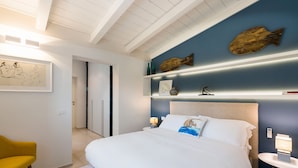 A modern bedroom with a large bed, a bedside table, a nightstand, a chair, and a wall with decorative fish and shelves. - Luxury villa with pool, beach front, Porto Ulisse (Ispica)