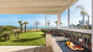A kitchen with a view of the sea, a tiled backsplash, and a countertop with fruits and bottles. - Luxury villa with pool, beach front, Porto Ulisse (Ispica)