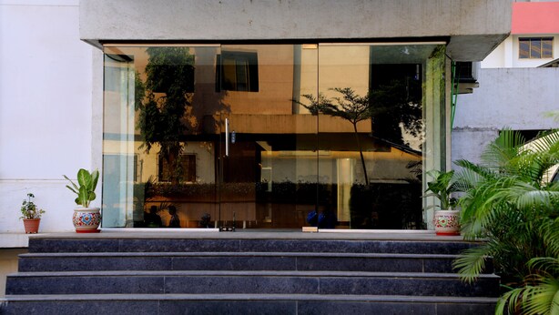A building entrance with a glass facade, steps leading up to it, and potted plants on the steps. - Silver Paradise (Navi Mumbai)