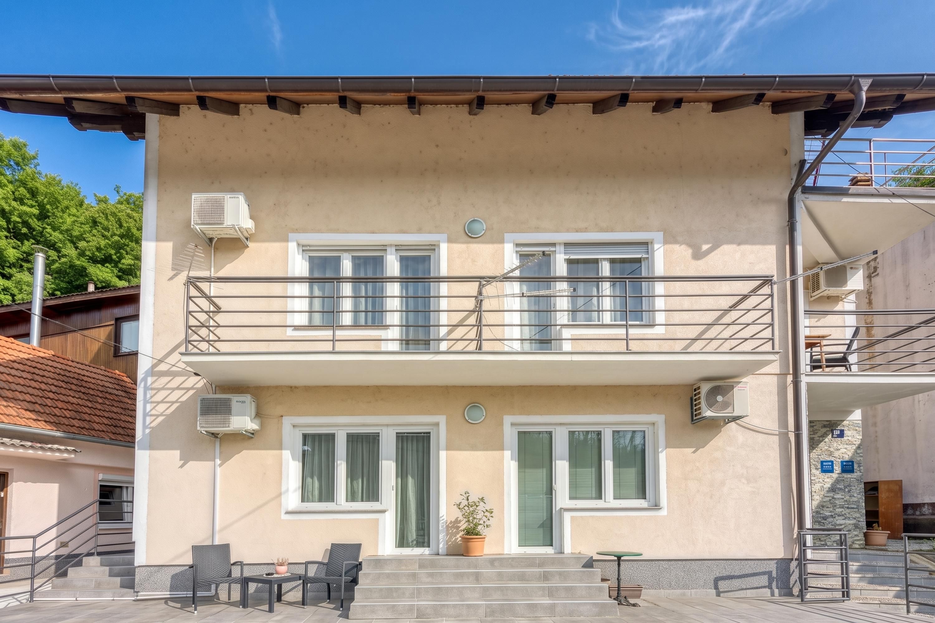 A two-story building with a balcony, air conditioning units, and a small outdoor seating area with chairs and a table.