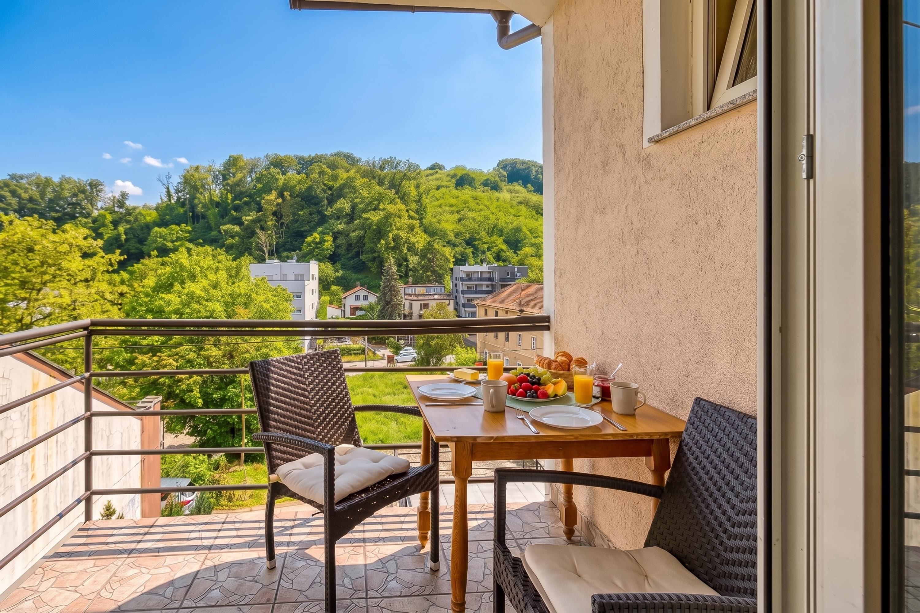 Un balcón con una mesa lista para el desayuno, con vistas a un paisaje verde.
