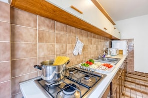 A modern kitchen with a gas stove, a pot of spaghetti, and a variety of fresh vegetables on the counter. - Green Hill Zagreb Apartments (Zagreb)