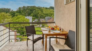 Un balcon avec une table dressée pour le petit-déjeuner, des chaises et une vue sur une colline verdoyante.