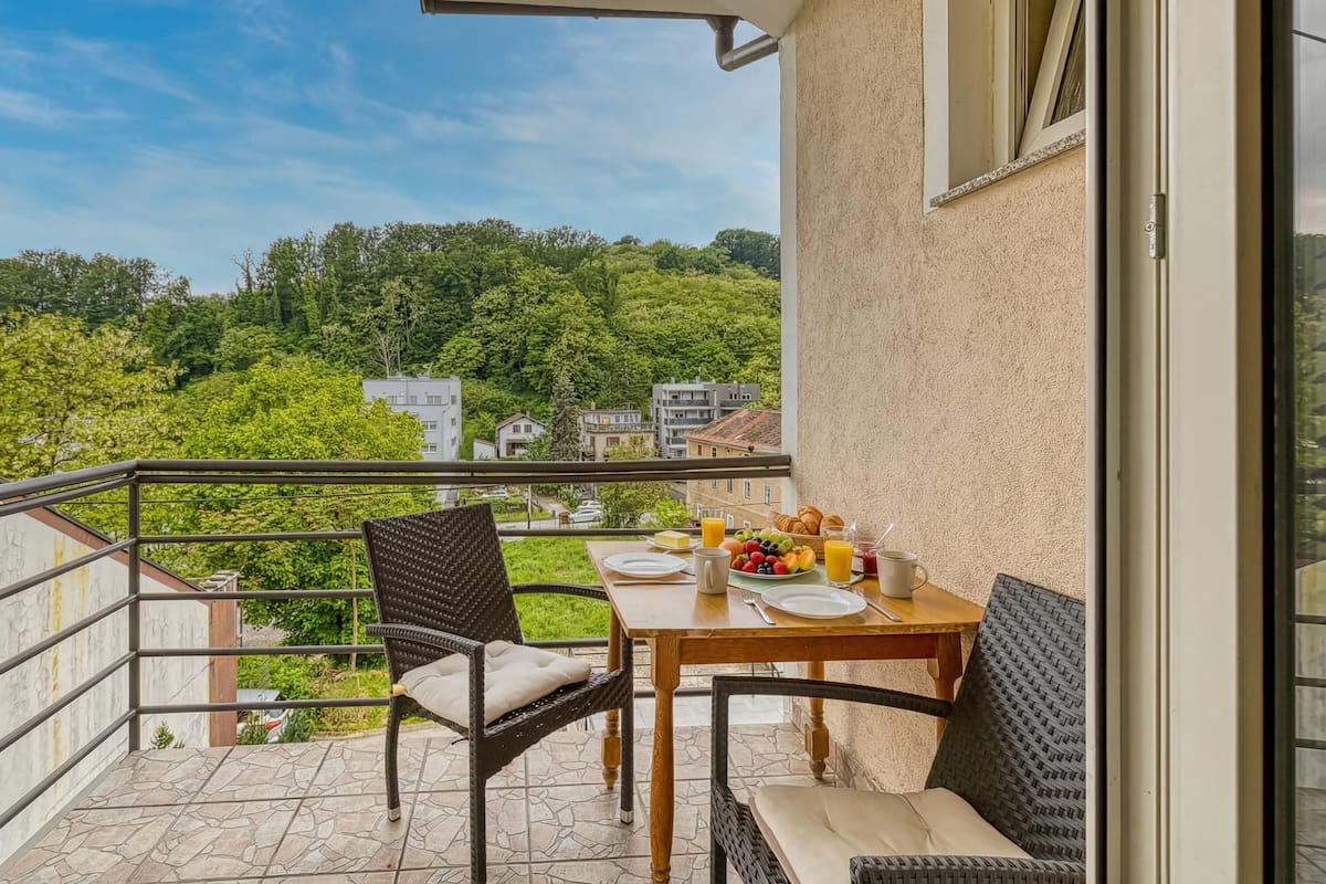 Een balkon met een ontbijttafel, stoelen en uitzicht op een groene heuvel.