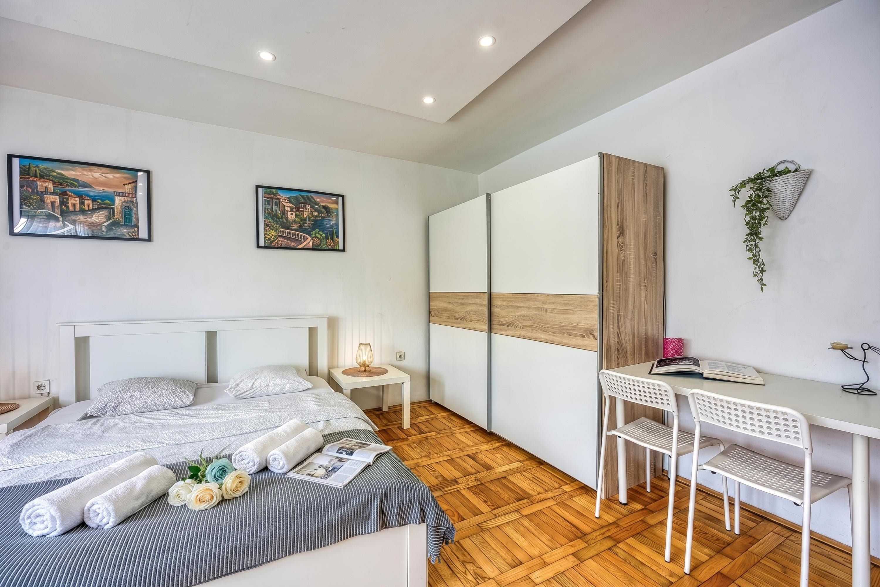A modern bedroom with a bed, a desk, and two paintings on the wall.