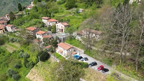 Un pueblo en una ladera con casas de piedra tradicionales, una carretera pavimentada y automóviles estacionados.