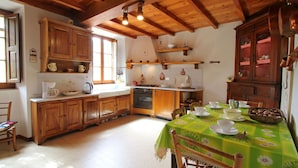 Una cocina con armarios de madera, una mesa de comedor con mantel floral y un ventanal que proporciona luz natural.
