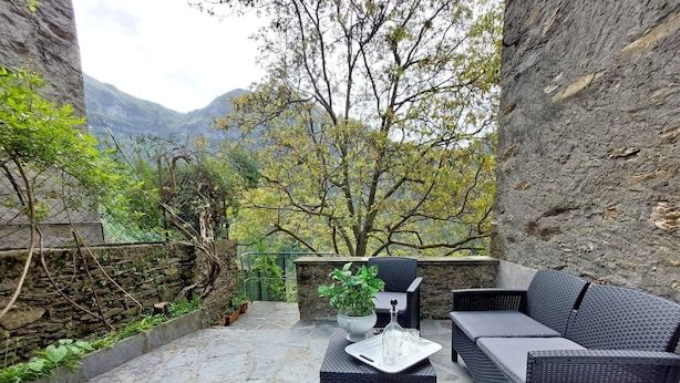 Un área de estar al aire libre con mobiliario de mimbre, un muro de piedra y vistas a las montañas.