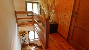 Una escalera de madera con barandilla, un jarrón con flores secas y una puerta con manija.