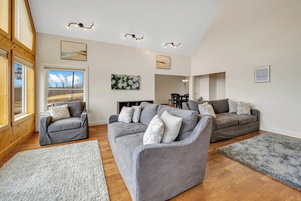 A spacious living room with two grey sofas, a wooden floor, and a large window.