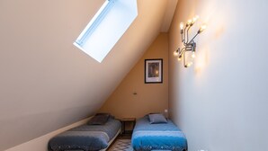 Un dormitorio acogedor en el ático, con dos camas, un tragaluz y una lámpara fijada a la pared.