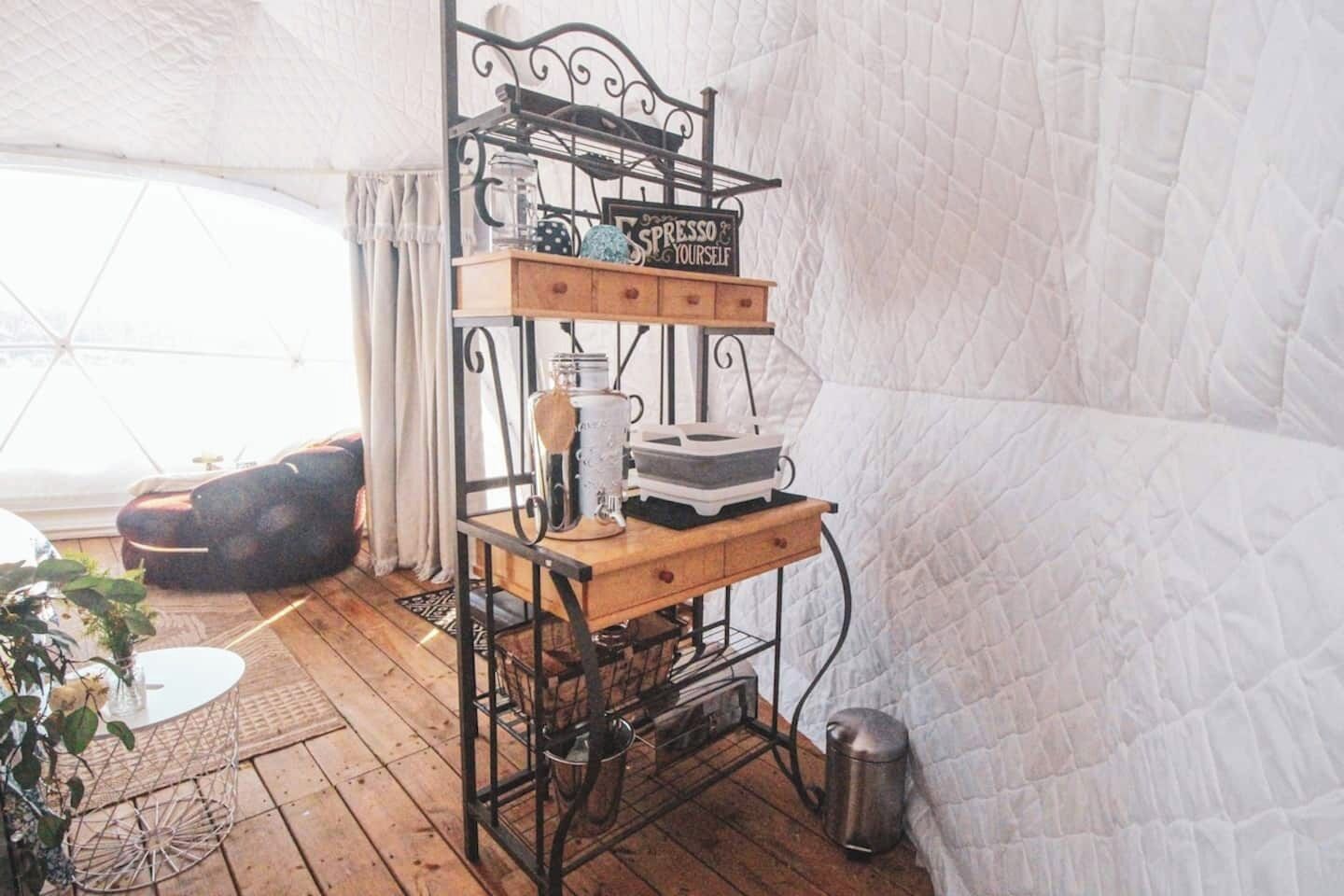 A cozy room with a wooden table, a metal shelf unit, and a white quilted wall.