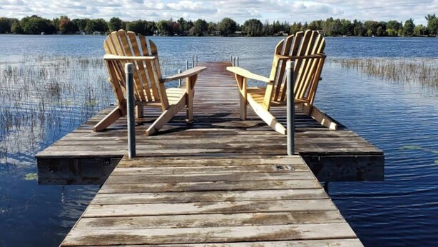 A wooden dock extending into calm water with two wooden chairs facing each other.