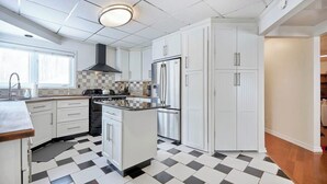 A kitchen with white cabinets, a black and white checkered floor, a central island, and a stainless steel refrigerator.