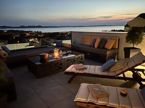 Eine Dachterrasse mit einer Couch, Liegestühlen und einem Tisch mit Kerzen.