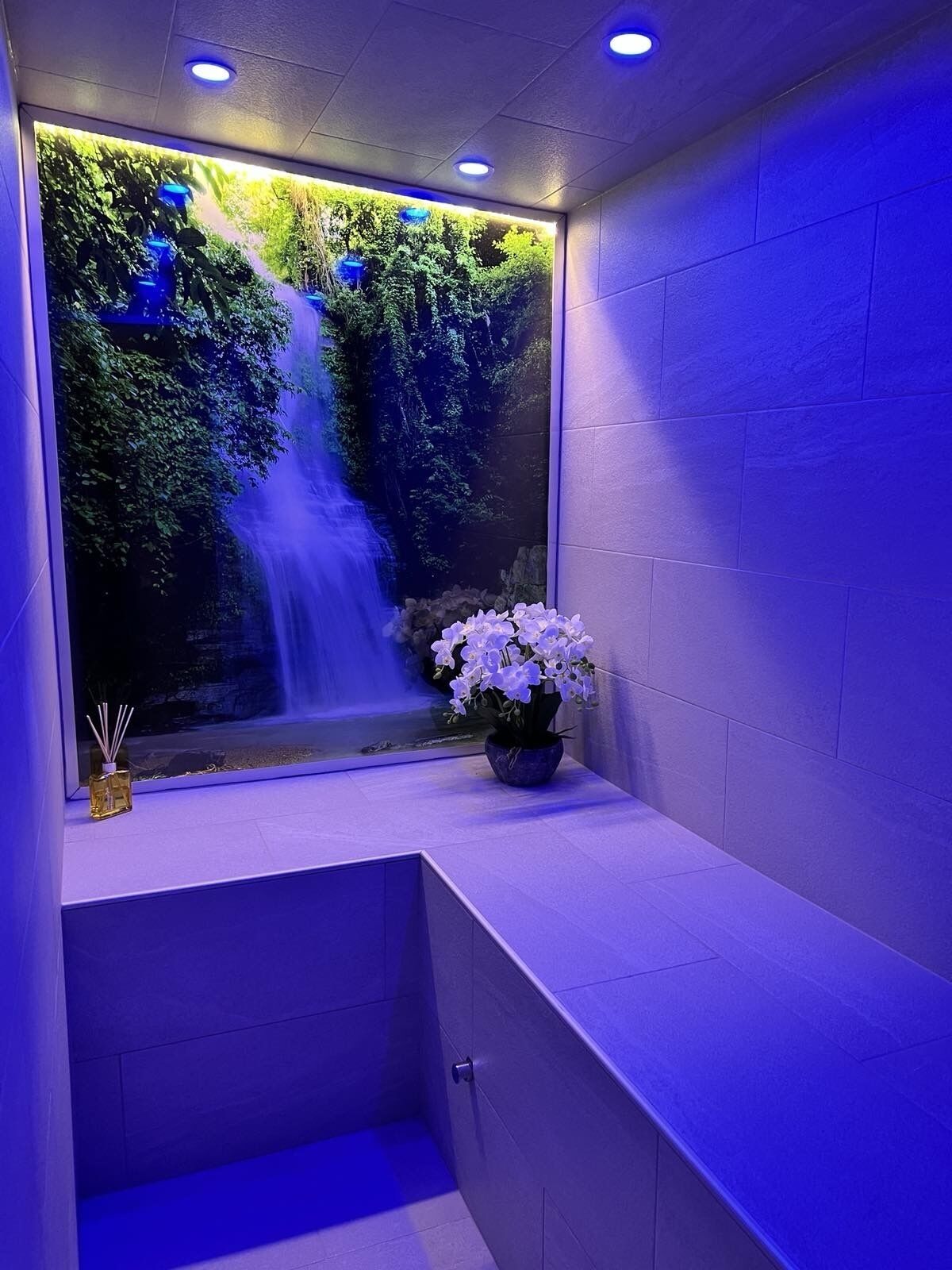 A bathroom with a built-in waterfall feature, a potted orchid, and a small bottle of reed diffuser.