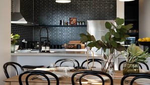 Une cuisine moderne avec un mur recouvert de carreaux noirs, un plan de travail en bois et un coin repas comprenant une table et des chaises en bois.