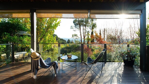 Une terrasse en bois avec deux chaises et une table, donnant sur un jardin arboré et offrant une vue sur le paysage.