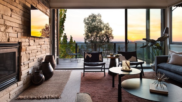 Un salon moderne avec une cheminée, un balcon doté d’un espace salon extérieur et une vue sur le coucher de soleil.