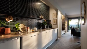 Une cuisine moderne avec un mur recouvert de carreaux noirs, un plan de travail sur lequel sont disposés divers objets, et une vue sur un balcon doté d’un mur en pierre.